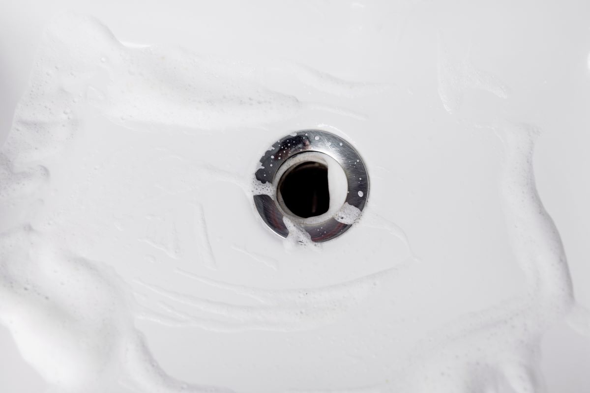 A white sink with soapy water swirling down a silver metal drain.