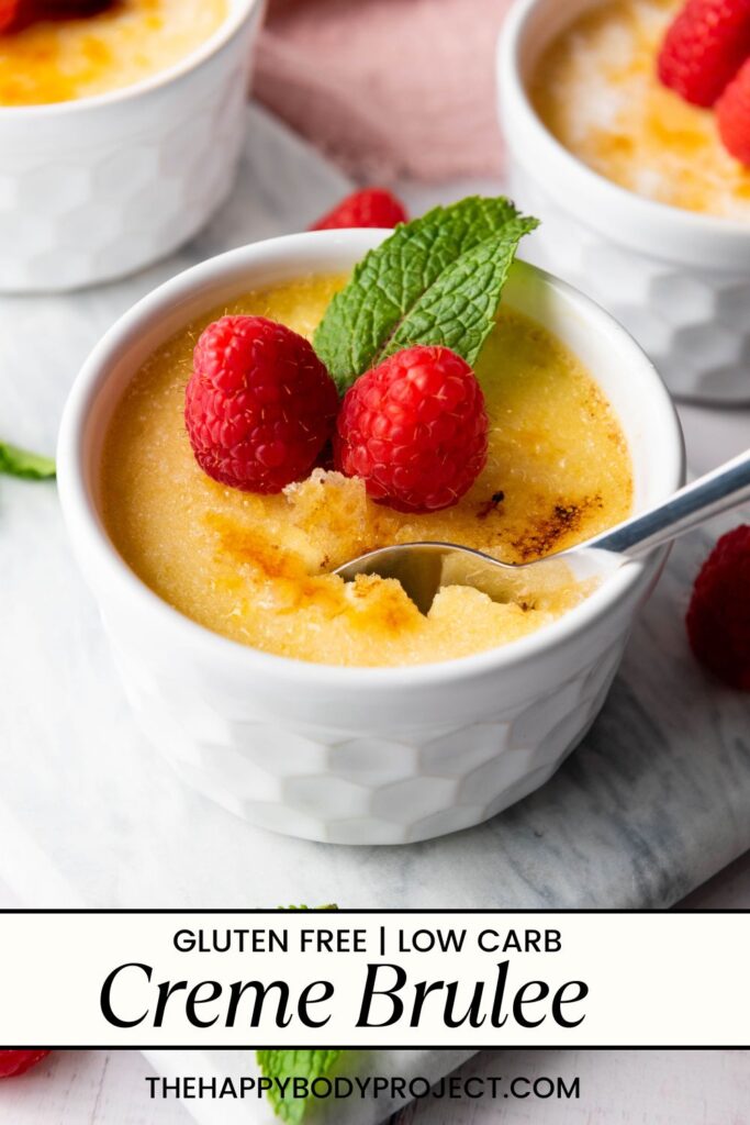 A small ramekin of crème brûlée topped with fresh raspberries and a mint sprig. A spoon dips into the creamy dessert. Text at the bottom reads, "Gluten Free | Low Carb Creme Brulee.