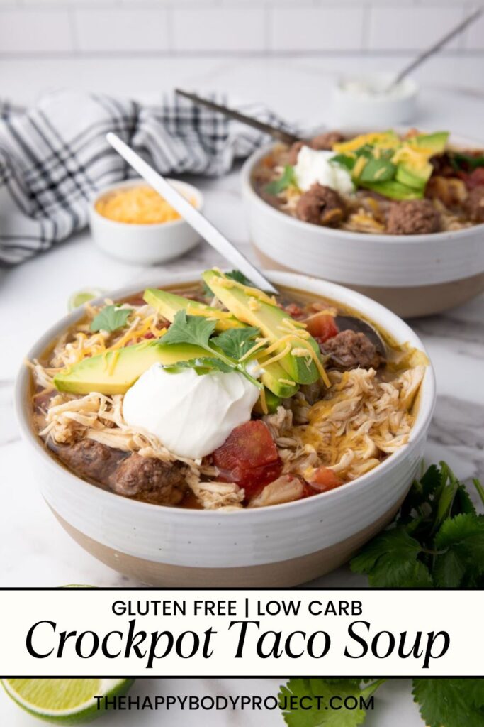 Two bowls of crockpot taco soup topped with avocado slices, sour cream, cheese, and cilantro sit on a table. A wedge of lime and a striped napkin are in the background. The text reads: "Gluten Free | Low Carb Crockpot Taco Soup.