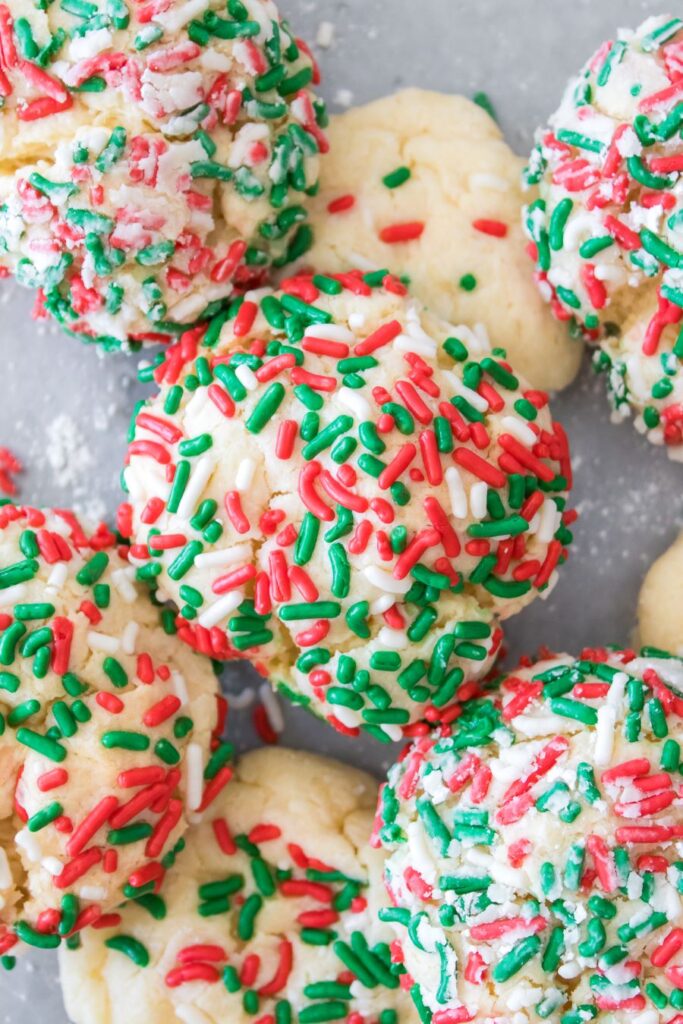 A close-up of festive cookies covered in red, green, and white sprinkles. The cookies are arranged on a gray surface, showcasing a soft, crumbly texture with plenty of colorful sprinkles.