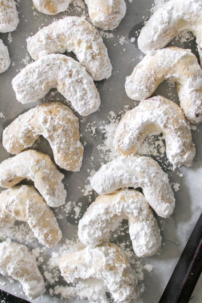 A tray of crescent-shaped cookies dusted with powdered sugar, arranged on parchment paper.