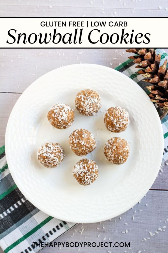 A white plate with seven snowball cookies covered in shredded coconut. The text above reads "Gluten Free | Low Carb Snowball Cookies." A pine cone and a green plaid cloth are visible nearby.