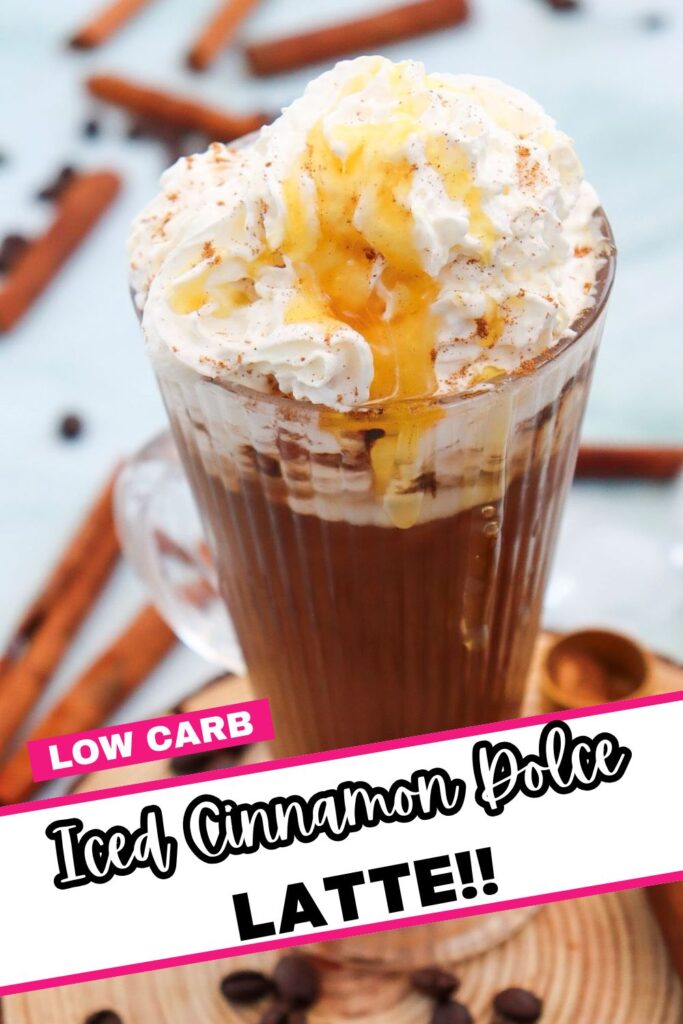 A glass mug filled with iced cinnamon dolce latte topped with whipped cream and caramel drizzle. Cinnamon sticks and coffee beans are scattered around. Bold text reads "Low Carb Iced Cinnamon Dolce Latte!!" in pink and black.