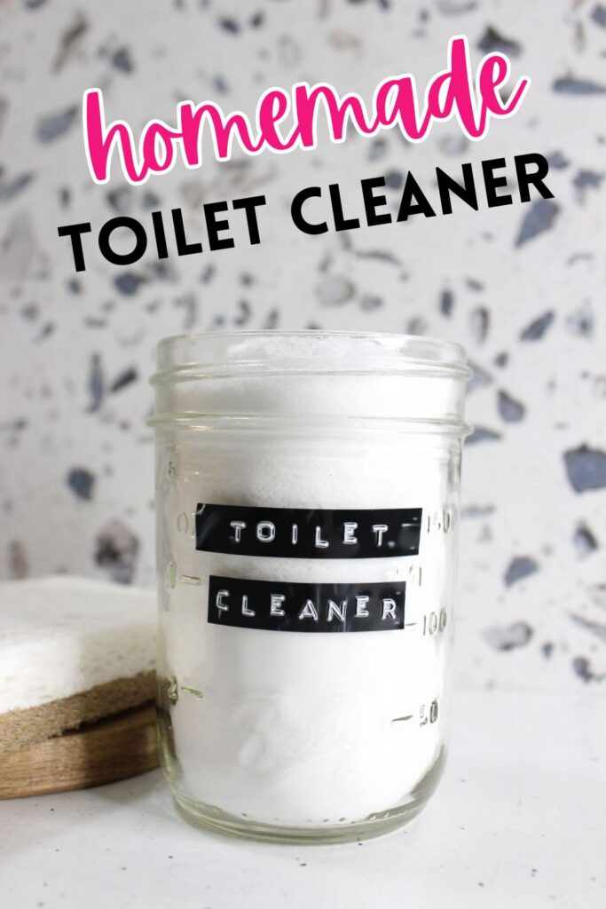 A glass jar labeled "TOILET CLEANER" contains a white powder. The background features a terrazzo surface with spots of different colors, and a sponge is partially visible next to the jar. The words "homemade toilet cleaner" are at the top.