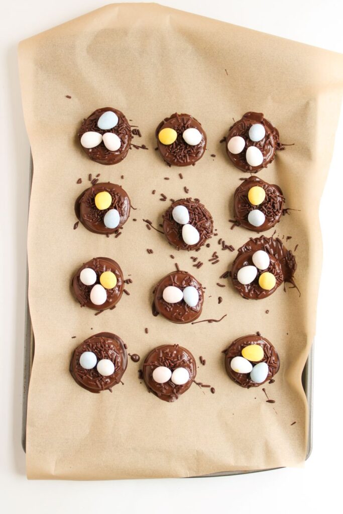 Chocolate cookies with colorful candy eggs and chocolate sprinkles are arranged on a baking sheet lined with parchment paper.