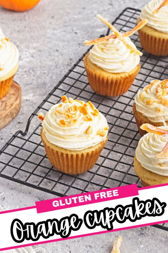 Five orange cupcakes with swirled frosting and orange zest sit on a cooling rack. Text at the bottom reads “Gluten Free Orange Cupcakes.” The background is a light gray surface.