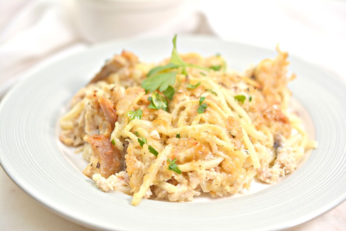 A close-up of a plate of creamy baked chicken spaghetti, garnished with chopped parsley and melted cheese, served on a white dish.
